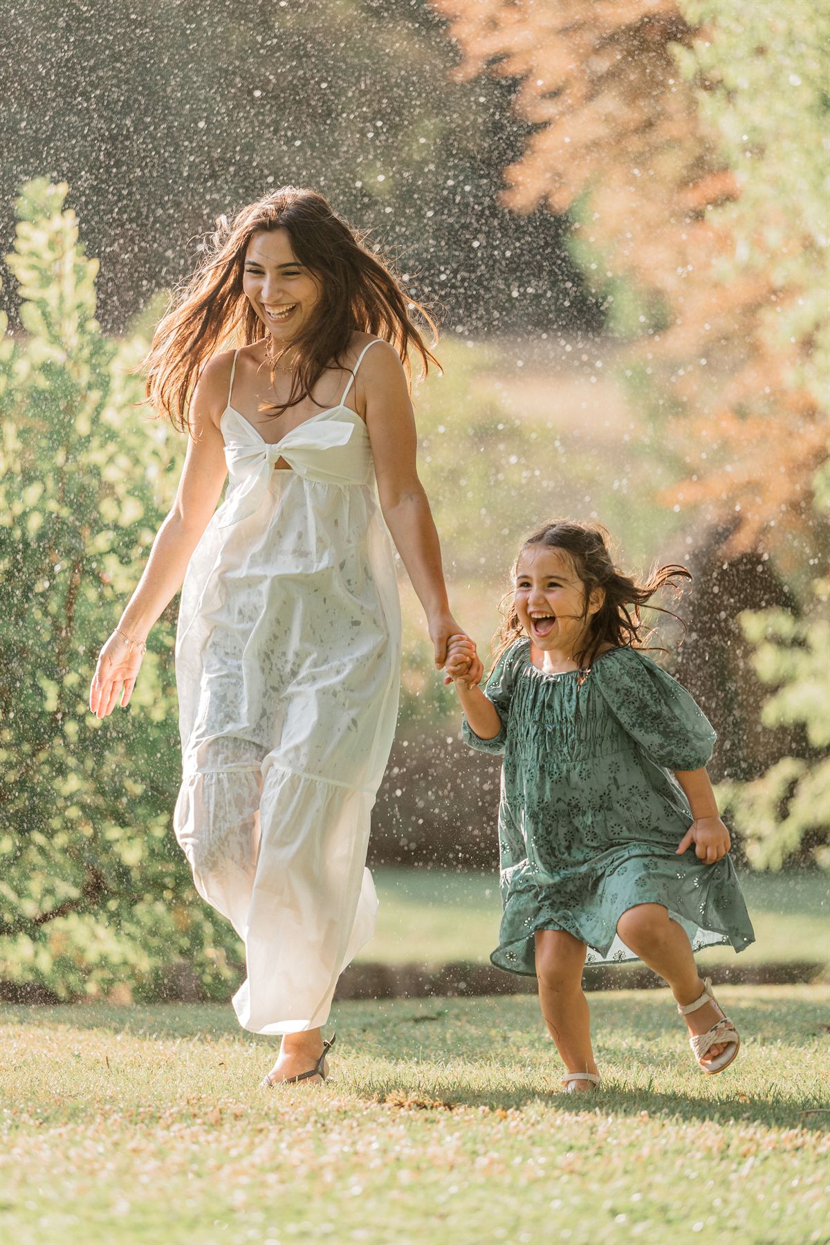 Maman et sa fille courant main dans la main sous des gouttes d'eau